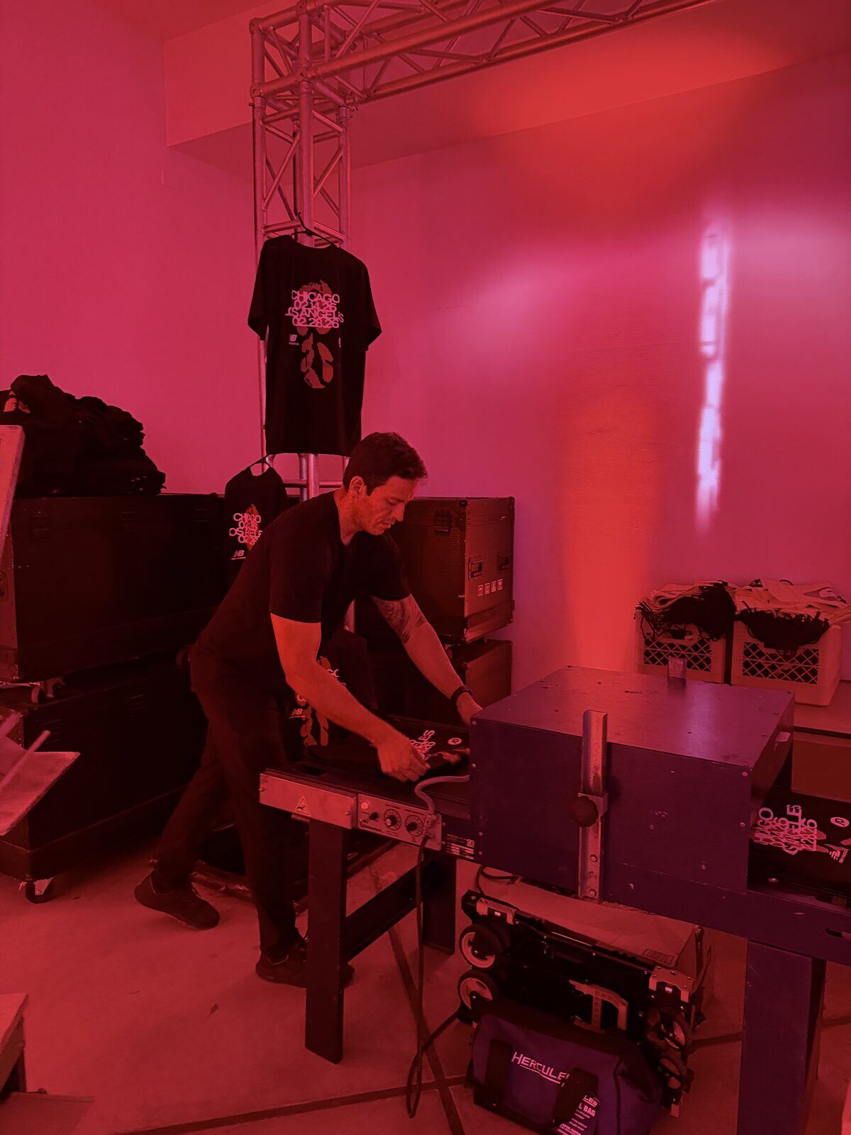 Merch Troop printer running shirts through a conveyor dryer in a backstage prep room lit red