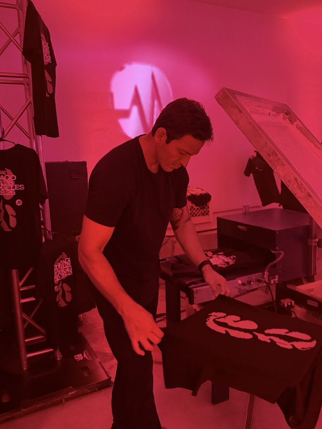Printer laying a shirt onto a heat press in a red-lit backstage production room