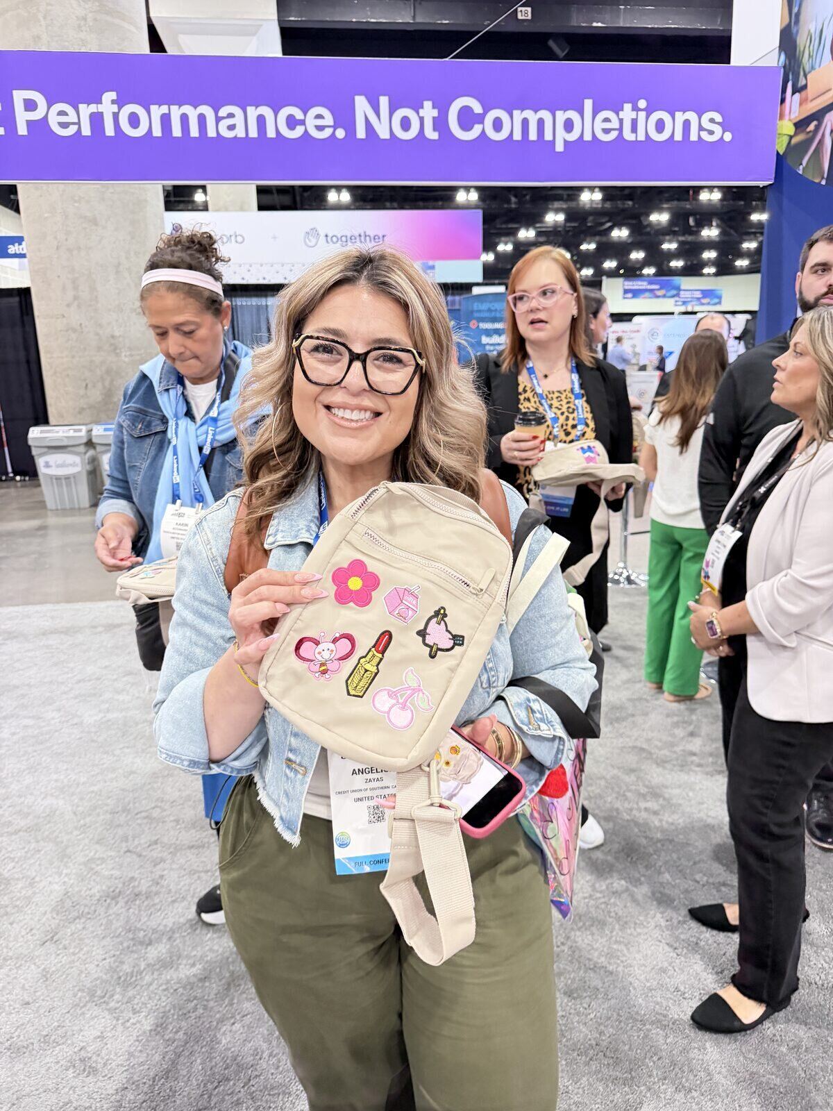 Smiling attendee showing off a crossbody bag decorated with pressed patches on a convention expo floor
