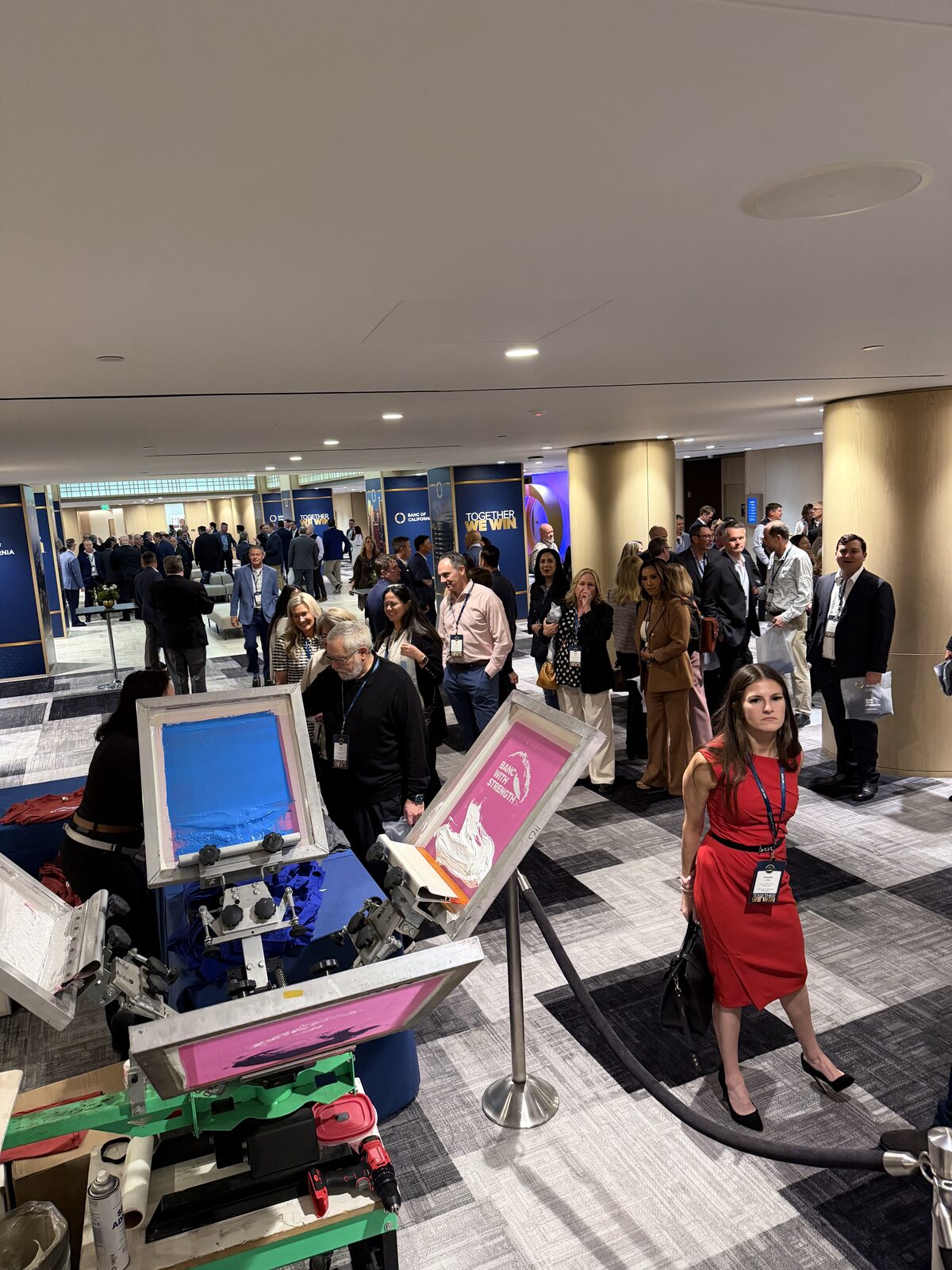 Attendees in business attire lining up at a live screen printing station during a corporate summit